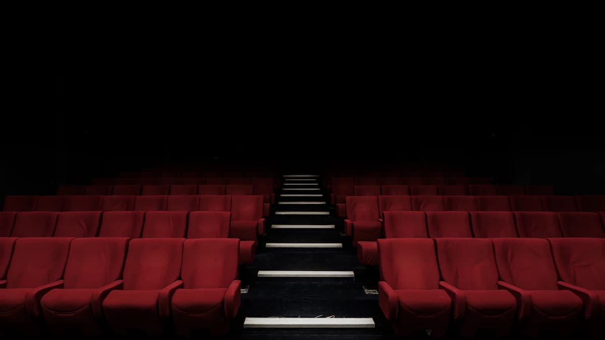 Inquadratura ravvicinata e d’effetto di una fila di sedie rosse vintage all’interno di un cinema deserto e buio